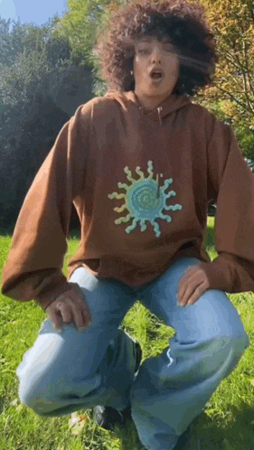 a person with curly hair wearing a brown hoodie and blue jeans