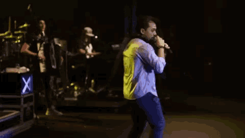 a man singing into a microphone on a stage in front of a sign that says x
