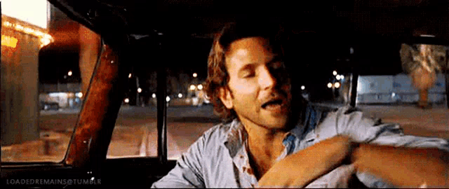 a man is sitting in the driver 's seat of a car at night and singing .