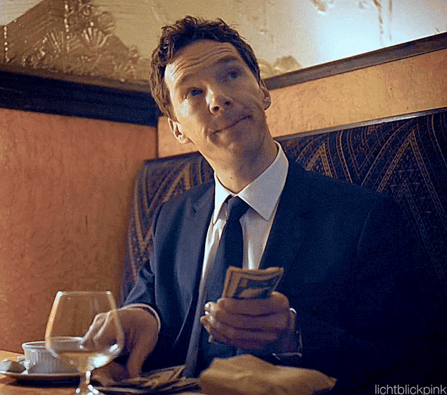 a man in a suit and tie is sitting at a table holding money