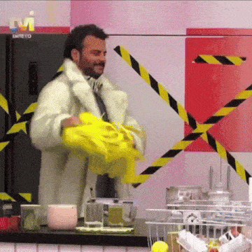 a man in a fur coat is holding a yellow shirt in front of a tv screen that says " direto "