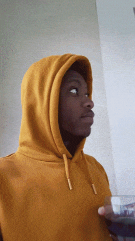 a person wearing a yellow hoodie holds a glass of wine