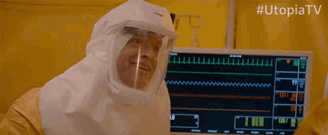 a man wearing a protective suit is smiling in front of a monitor that says utopia tv