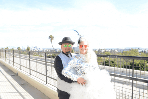 a man in a hat holds a woman in a white dress and sunglasses