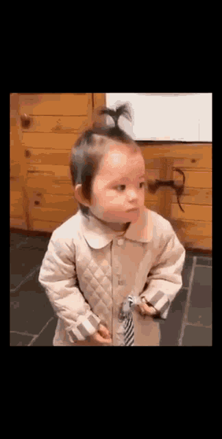 a baby is standing in front of a wooden wall and making a funny face .