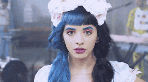 a woman with blue hair and blue eyebrows is wearing a white dress and a flower headband .