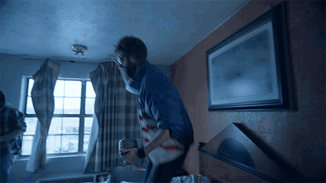a man in a blue shirt is standing in a bedroom