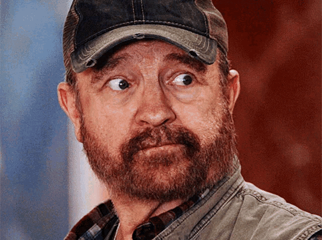 a man with a beard wears a hat and a vest