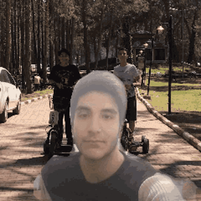 a man wearing a black hat is standing next to a man riding a scooter