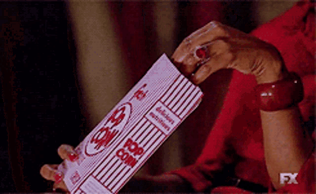 a woman in a red dress is holding a box of popcorn with the fx logo on the bottom