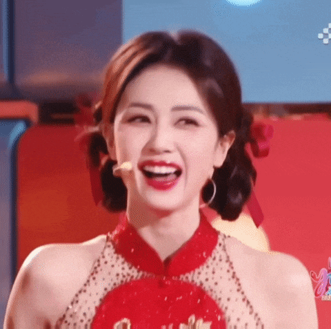 a woman in a red dress is smiling and looking at the camera with her mouth open .