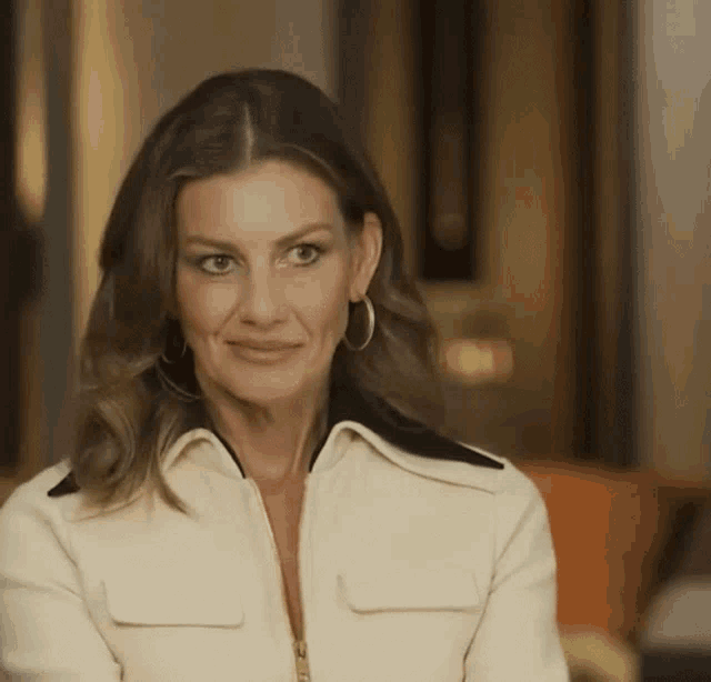 a woman is wearing a white jacket and hoop earrings .