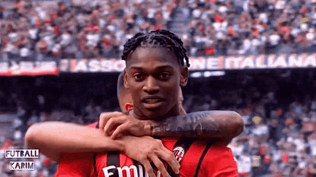 a soccer player wearing a red emirates shirt is hugging another player