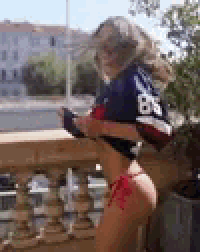 a woman in a bikini is standing on a balcony wearing a jersey with the number 86 on it .