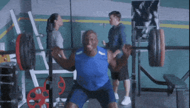 a man squatting on a barbell in a gym while a woman watches