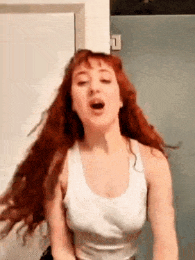 a woman with red hair is wearing a white tank top and dancing in a bathroom .
