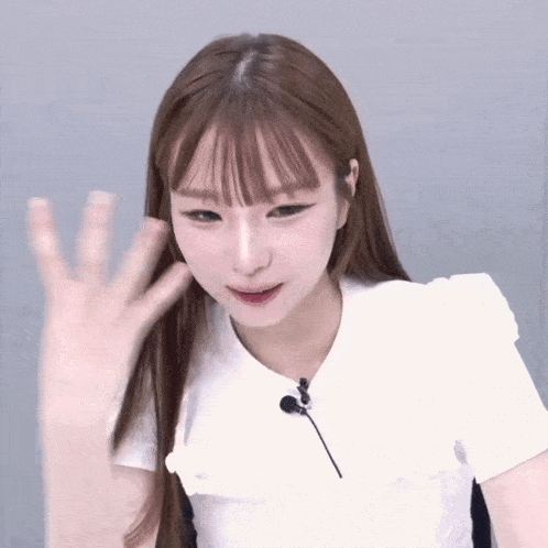 a woman wearing a white shirt with a microphone on it waves her hand