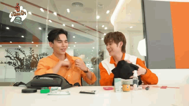 two men are sitting at a table with a balenciaga bag in front of them .