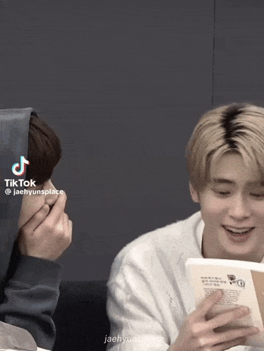 a man is reading a book while another man covers his face with his hand