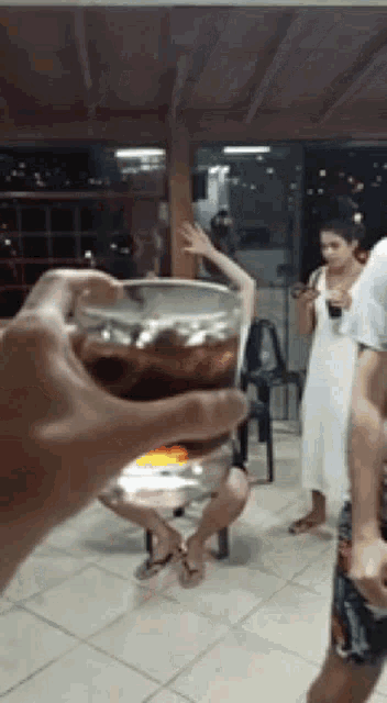 a person is holding a glass of cola in front of a group of people dancing .