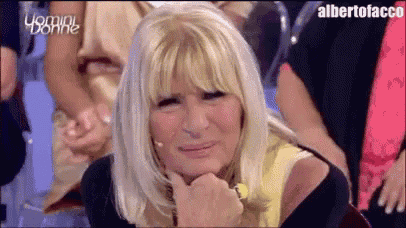 a woman with blonde hair is sitting in a crowd with her hand on her face .