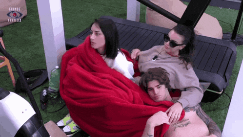 three people wrapped in red blankets are laying on a treadmill with grande fratello written on the bottom