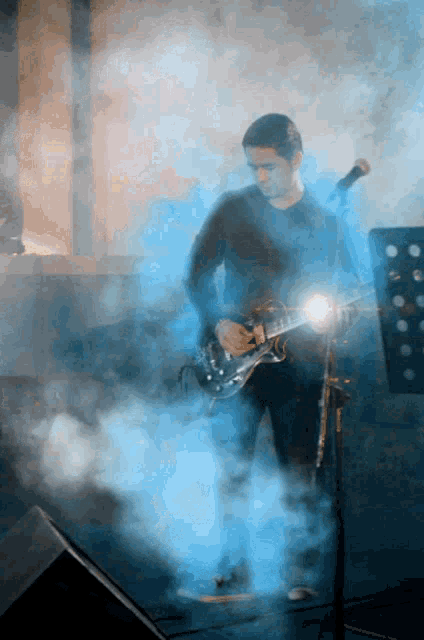 a man playing a guitar in front of a microphone in a foggy room