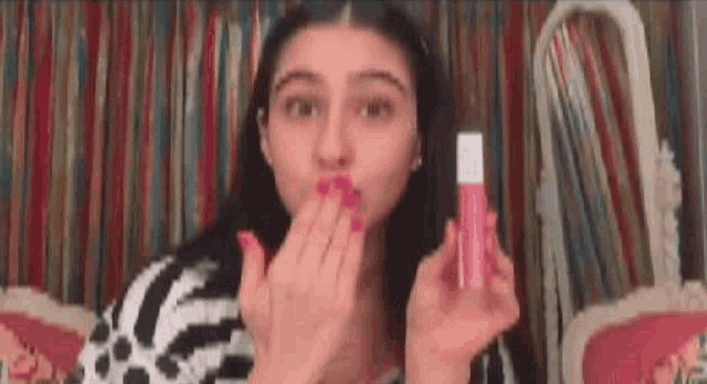 a woman is blowing a kiss while holding a bottle of pink lipstick .