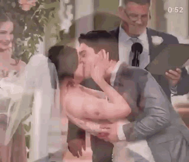 a bride and groom kissing at their wedding ceremony while a man holds a microphone .