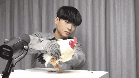 a man is holding a white chicken in front of a microphone and a white table .
