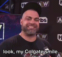 a man with a beard is smiling in front of a wall that says look my colgate smile .