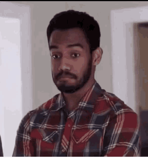 a man with a beard is wearing a plaid shirt and making a face .