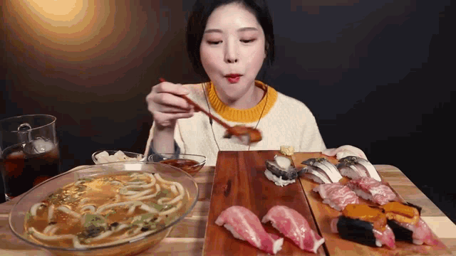 a woman is eating noodles and sushi with chopsticks at a table