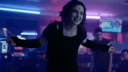 a woman is dancing in a dark room with her arms outstretched and smiling .