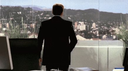 a man in a suit is standing in front of a window looking out at a city .