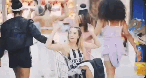 a woman is pushing another woman in a shopping cart in a crowded mall .