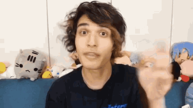 a man with long hair is sitting on a blue couch with stuffed animals .
