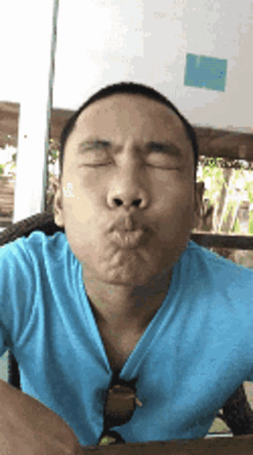 a man wearing a blue shirt is blowing a kiss