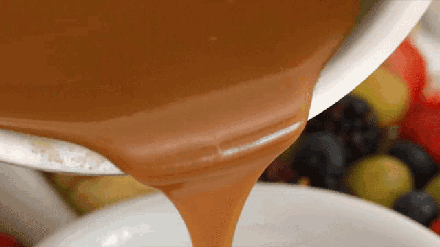 caramel sauce is being poured into a bowl filled with fruit