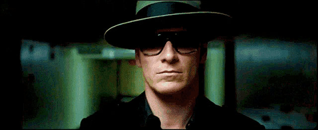 a man wearing a hat and sunglasses is standing in a hallway .