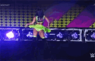 a woman in a green top and shorts is dancing on a stage in front of a sign that says wwe