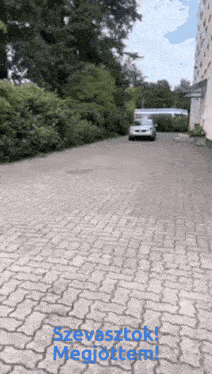 a car is driving down a brick driveway with the words szevasztok megjotterem written on the bottom