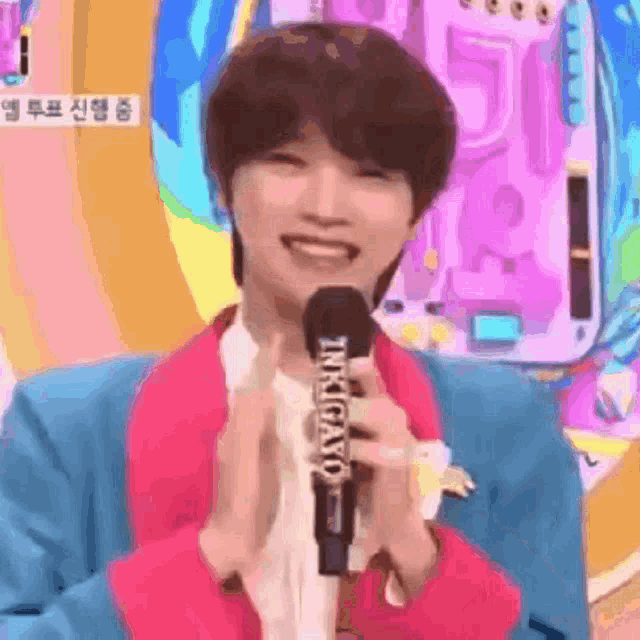 a young man in a pink jacket is holding a microphone .