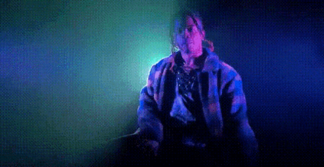 a man in a plaid jacket is singing into a microphone in front of a blue and green light .