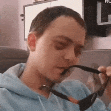 a man wearing a blue hoodie is holding a pair of sunglasses .