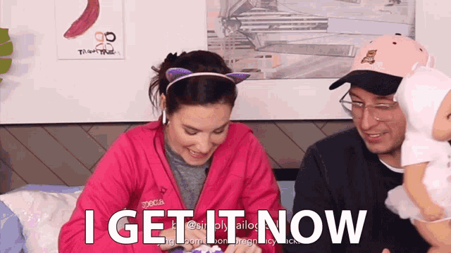 a woman in a pink jacket says " i get it now " while a man holds a baby doll