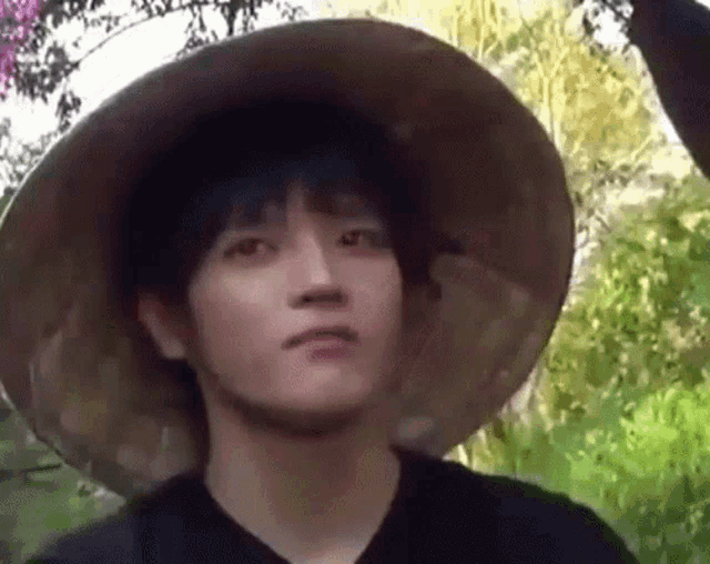 a young man wearing a conical hat is standing in the woods .