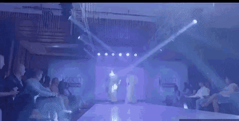 two models are walking down a runway at a fashion show while a crowd watches .