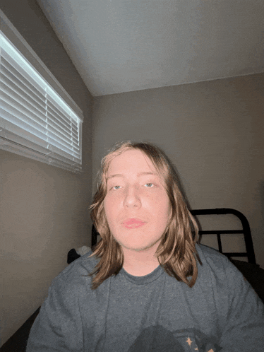 a young man with long hair is sitting on a bed in front of a window