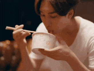 a young man is eating noodles with chopsticks from a bowl .